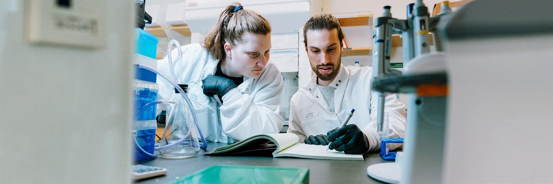 Two scientists wearing lab coats collaborate in the ISC web labs.